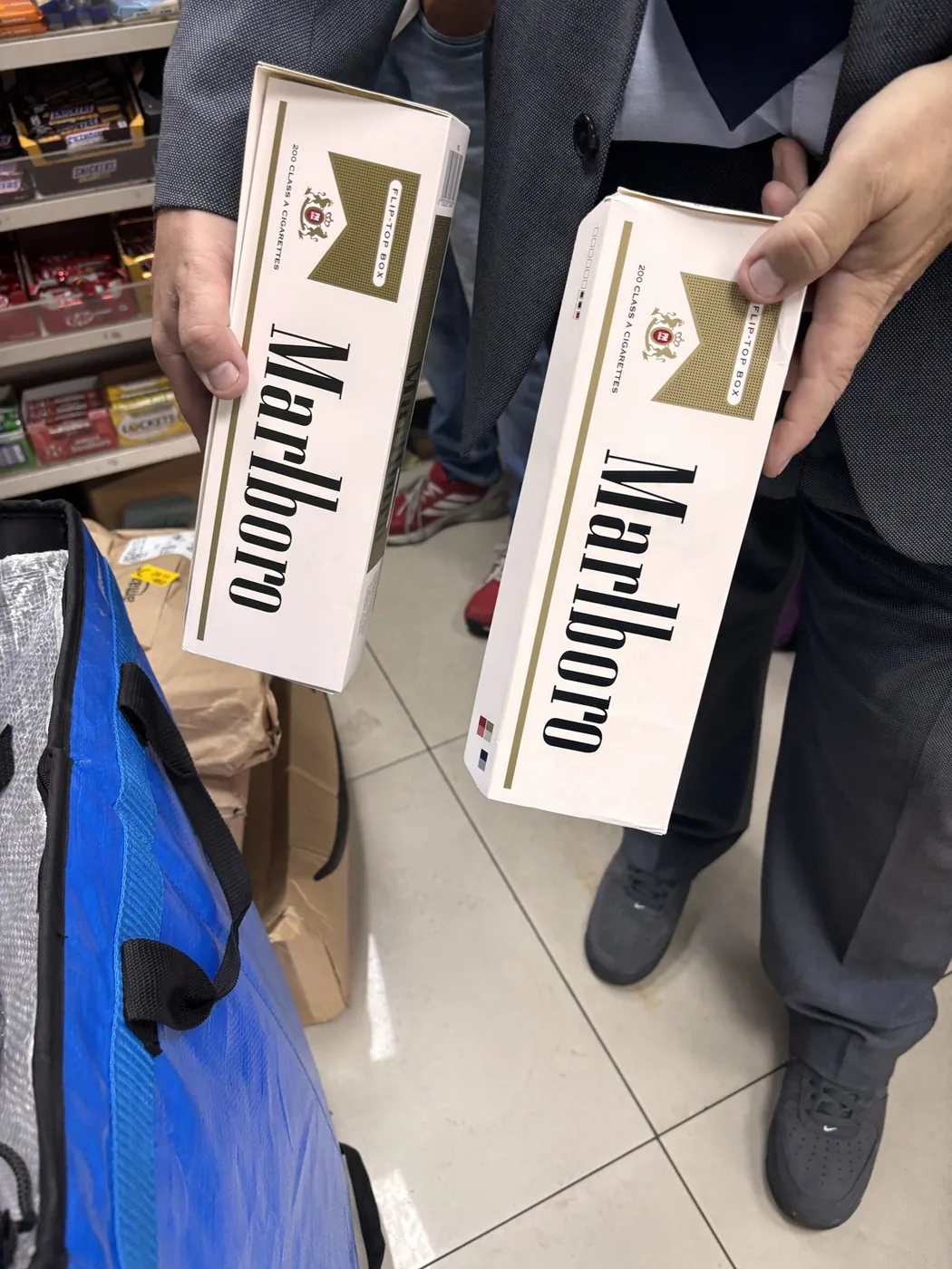 Two large cartons of Marlboro cigarettes, each marked 200 cigarettes, held up inside a shop